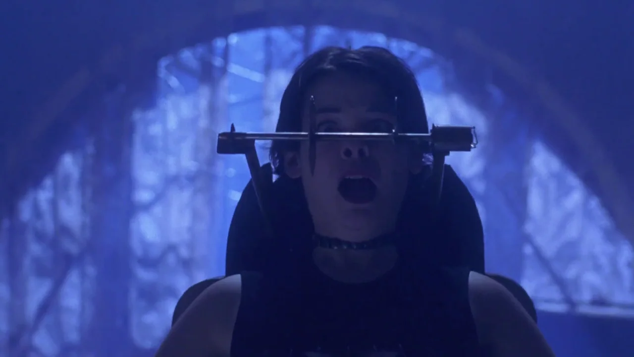 Hellraiser: Hellworld (2005) movie still: closeup — A young woman is trapped in a head-clamping metal device in a dimly lit space. She gazes forward…