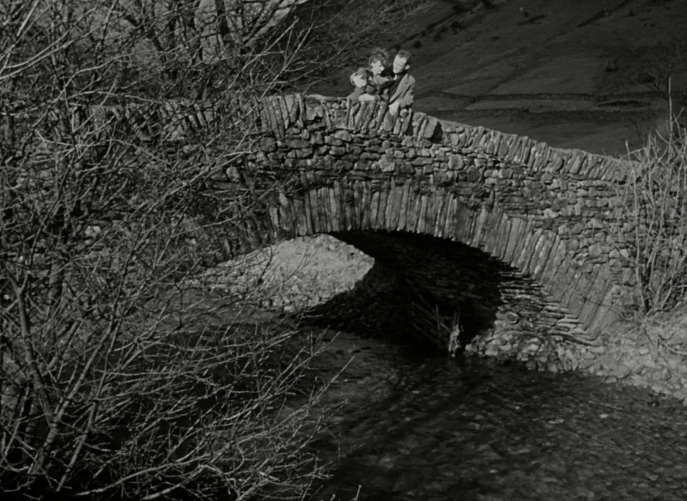 Brief Encounter (1945) movie still: wide — A rustic stone bridge spans a dark, narrow stream in a rural valley setting. A man and woman stand on the…