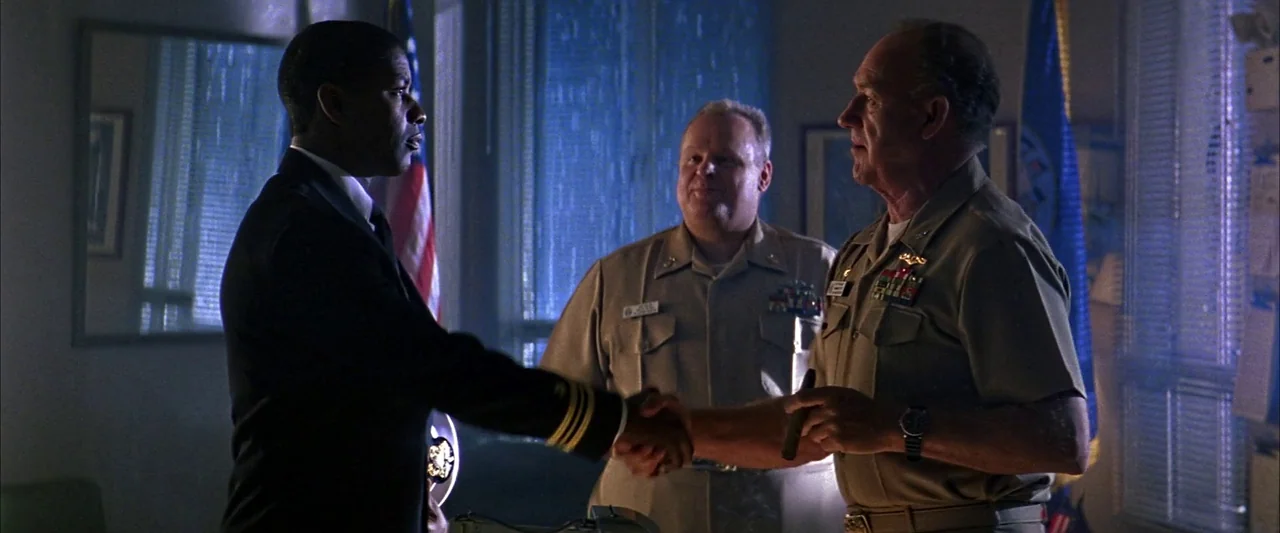 Crimson Tide (1995) movie still: medium — A dark military office is illuminated by blue moonlight coming through horizontal window blinds. Two men…