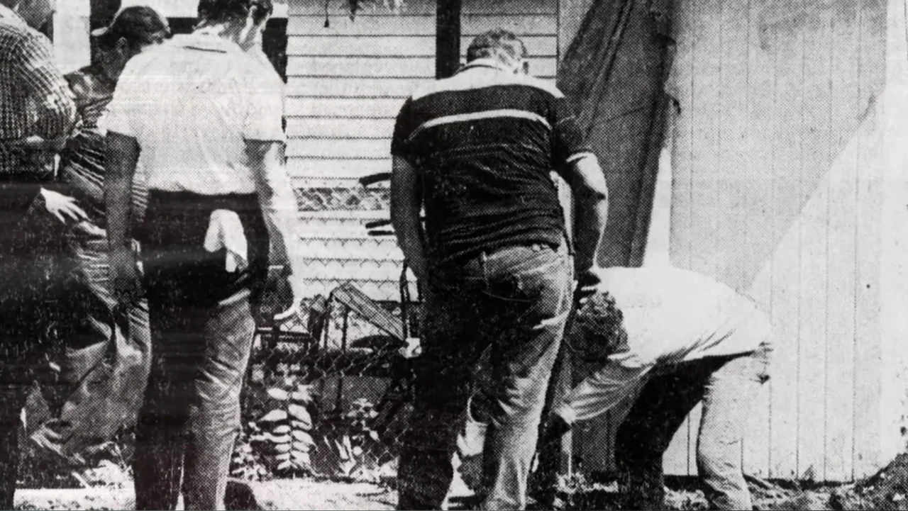 Murders at the Burger Joint (2022) movie still: fullbody — A residential yard with a wooden fence and chain link boundary. Four men stand together…