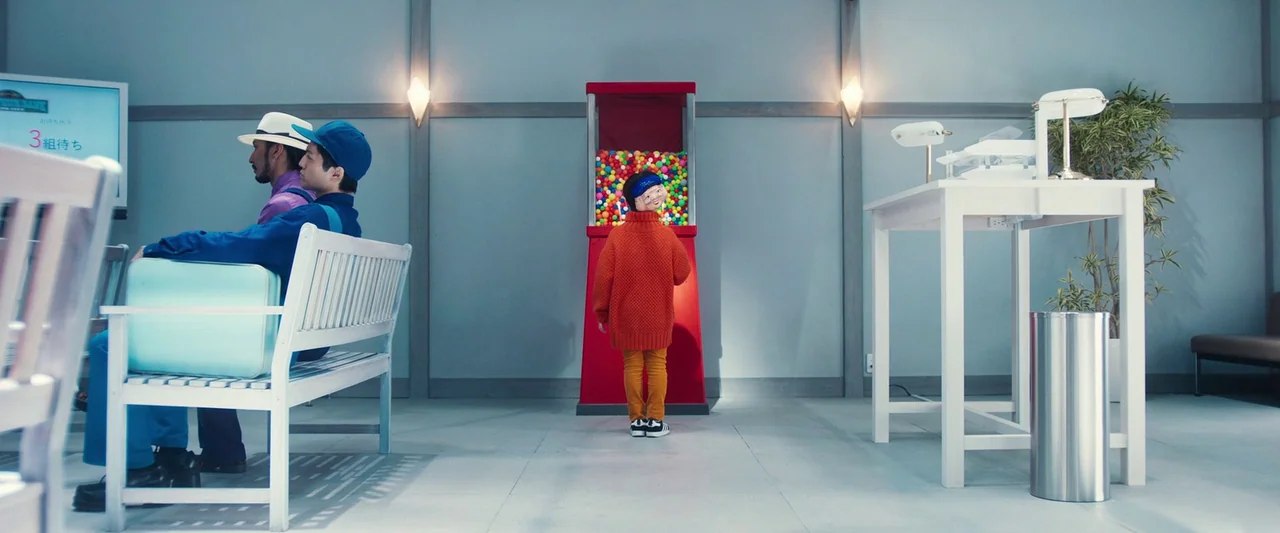 Prisoners of the Ghostland (2021) movie still: wide — A sterile, minimalist room features a white bench and a large red gumball machine. Three…