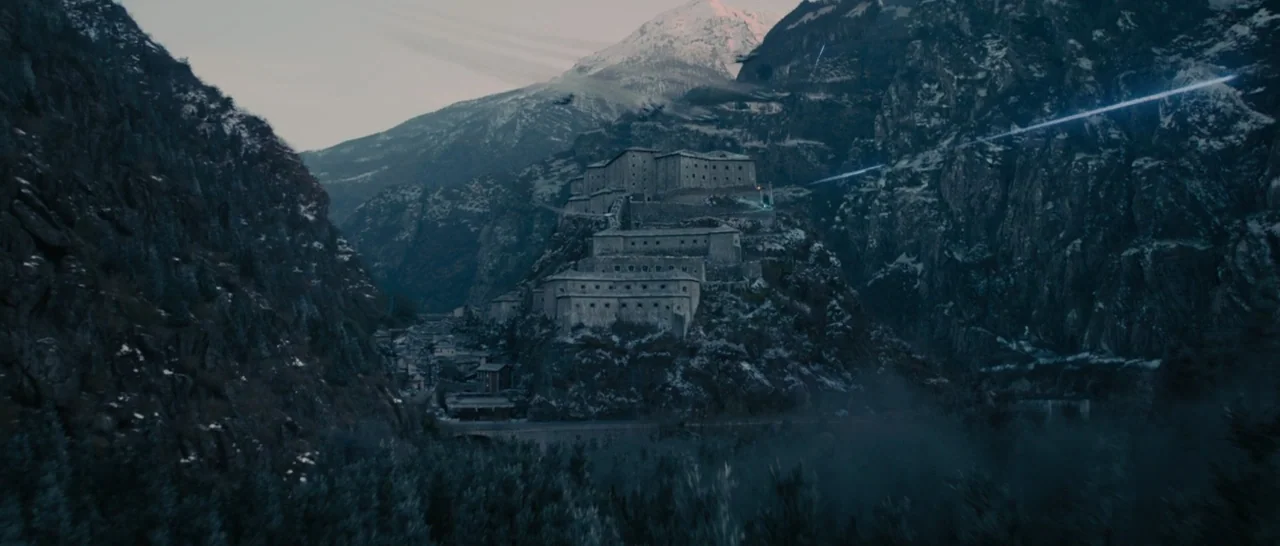 Avengers: Age of Ultron (2015) movie still: establishing — A massive stone fortress sits atop a steep, snow-dusted mountain cliff at dusk. Bright…