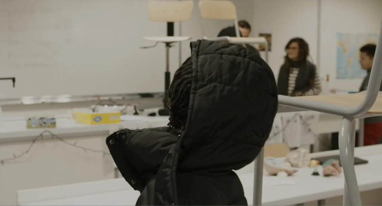 A Dramatic Film (2019) movie still: medium — A science classroom contains white lab tables with chairs stacked on top. Several students stand in the…
