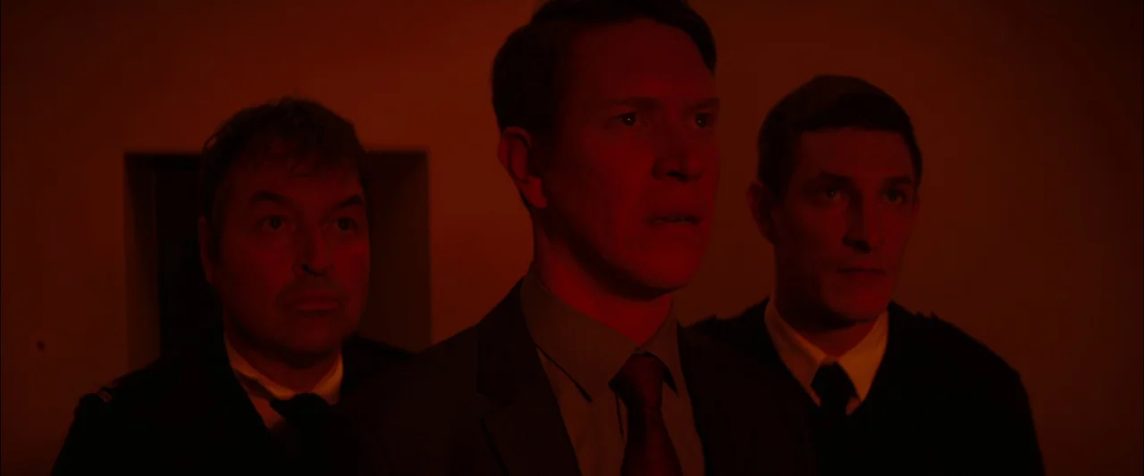 Starred Up (2013) movie still: medium — Three men stand close together in a darkened space illuminated by intense red light. They look toward the…