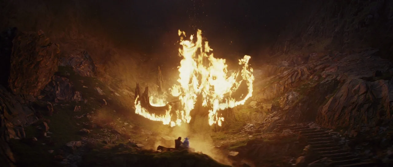 Star Wars: The Last Jedi (2017) movie still: wide — A deep rocky valley is illuminated by a towering, roaring bonfire at its center. The dark stone…