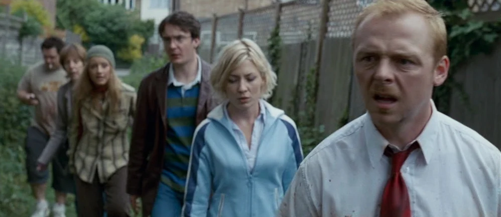 Shaun Of The Dead (2004) movie still: medium — A group of six people walk along a narrow dirt path bordered by fencing. The people display…