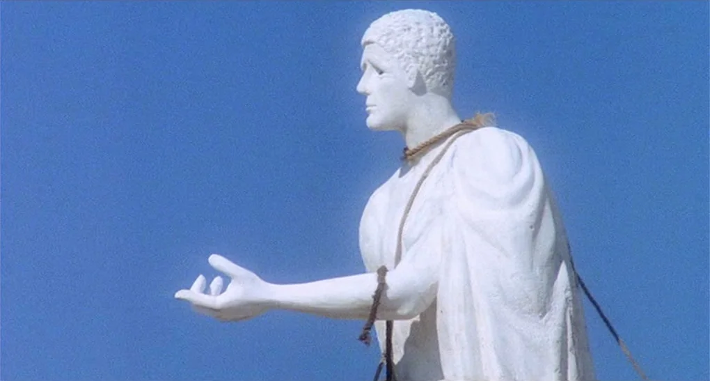 Life of Brian (1979) movie still: medium — A white stone statue stands against a clear, solid blue sky background. The statue is positioned in…