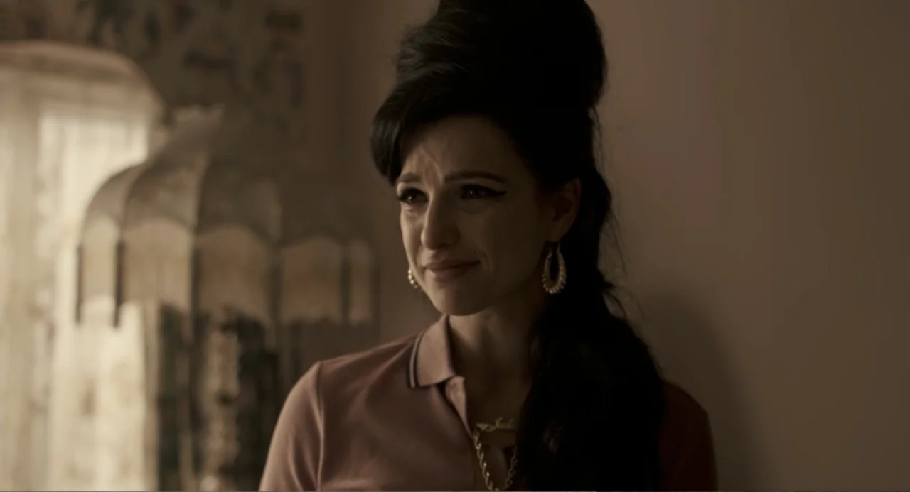 Back to Black (2024) movie still: medium — A dimly lit interior space with a blurred vintage lamp visible in the background. A woman with a 1960s…