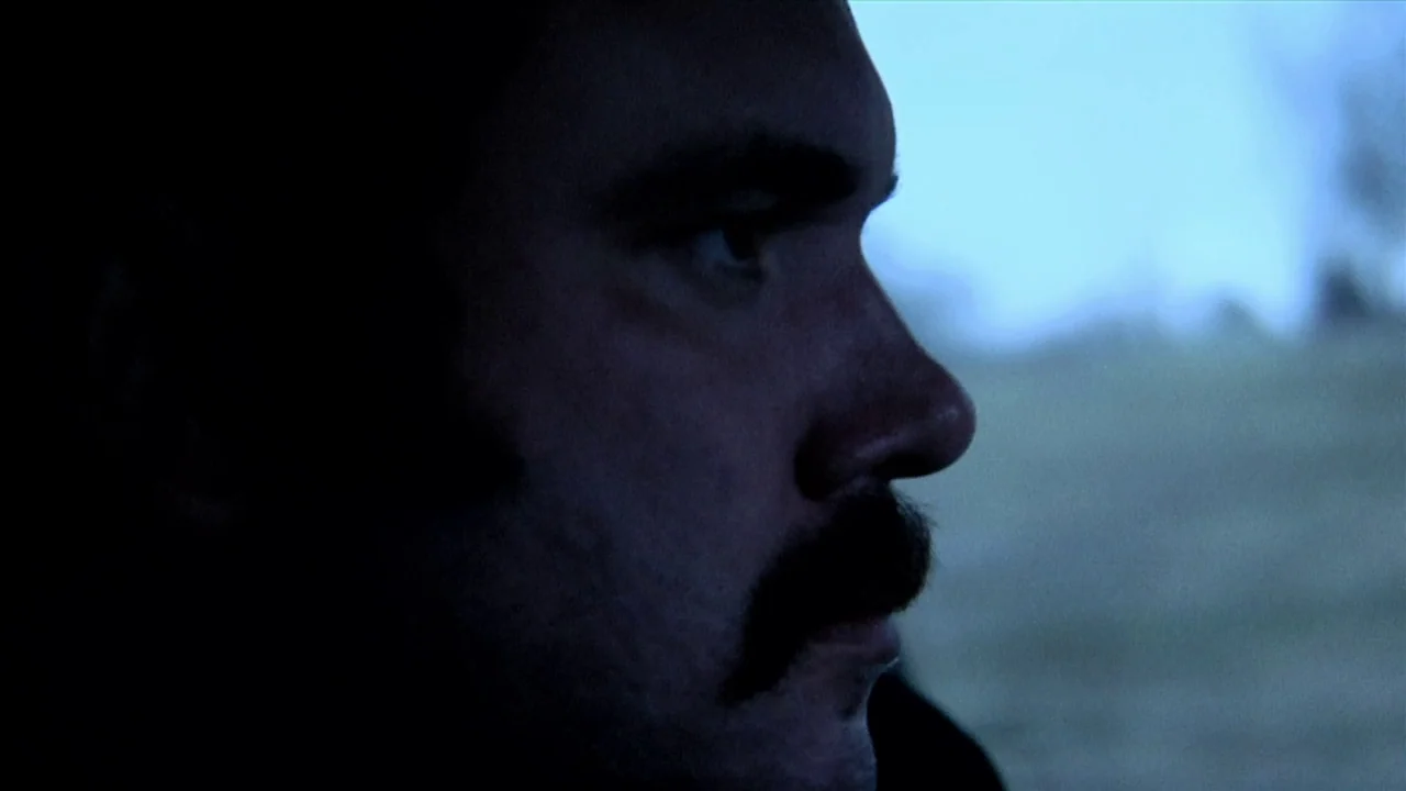 A Horrible Way To Die (2010) movie still: closeup — A man sits inside a vehicle while looking out the side window. The exterior background is…