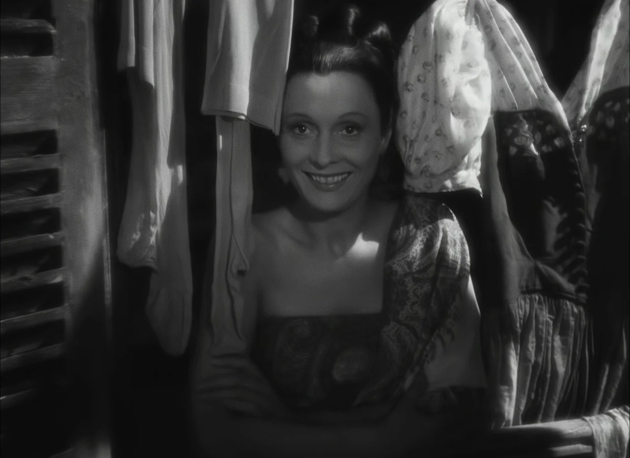 Les Enfants Du Paradis (1945) movie still: medium — A dark space filled with various articles of clothing hanging on rods. A woman stands in the…