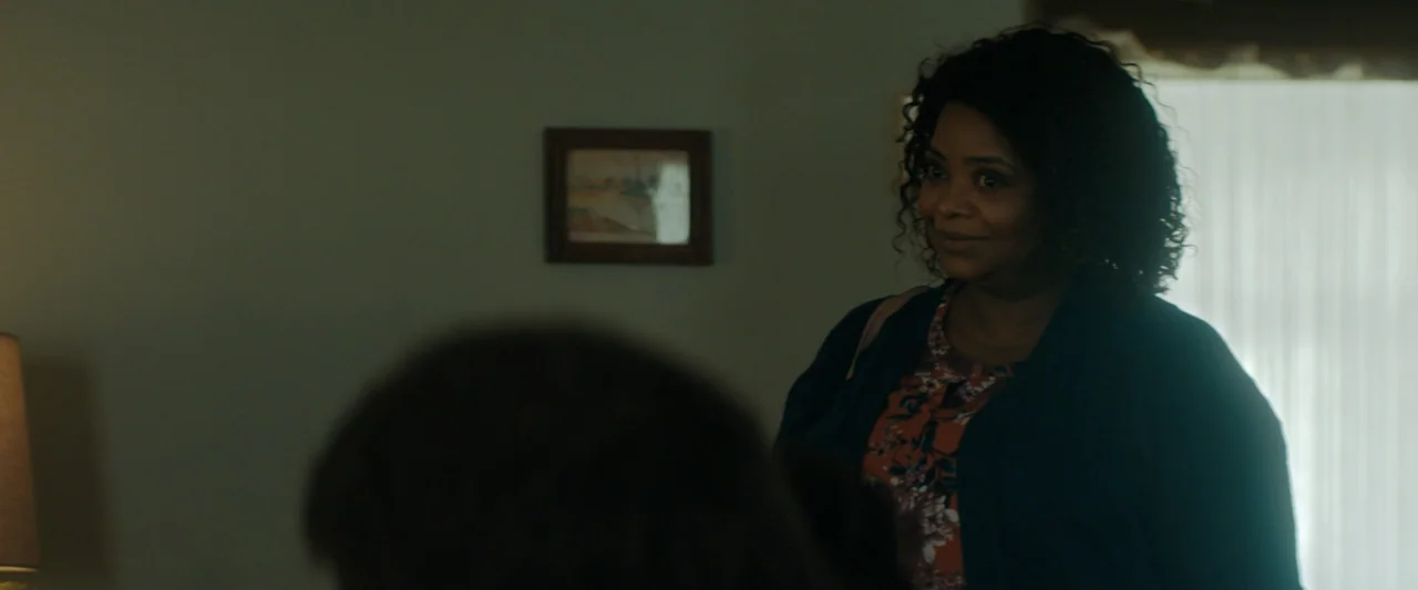 Encounter (2018) movie still: medium — A residential interior features a plain wall with a small framed picture hanging centered. A woman in a dark…