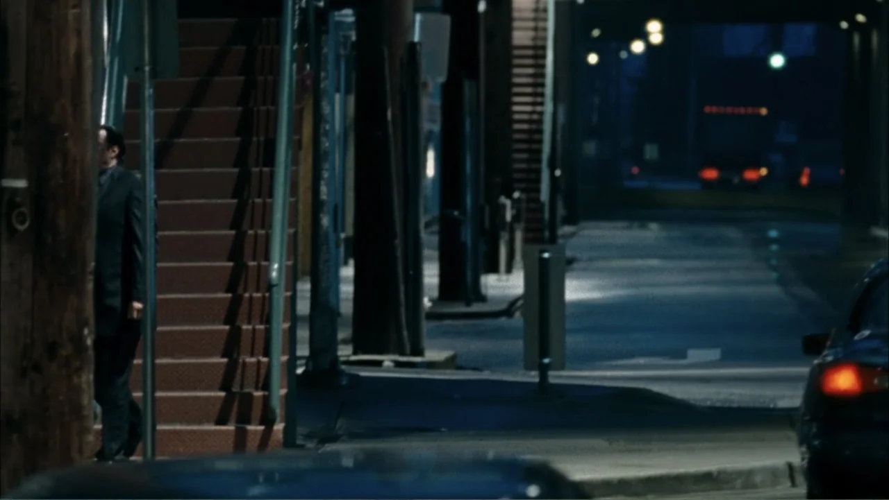 Driven to Kill (2009) movie still: wide — A dark city street at night features concrete infrastructure and a recessed stairwell entrance. A man in a…
