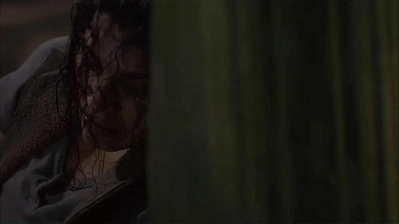 Ghost Ship (2002) movie still: closeup — A dimly lit room features a dark vertical partition obscuring part of the frame. A person with dark wet…