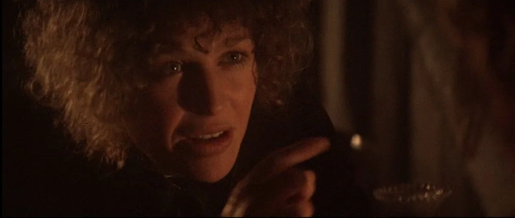 McCabe & Mrs.Miller (1971) movie still: closeup — A dimly lit room provides the backdrop for a close-up on a woman. The woman stares forward and…