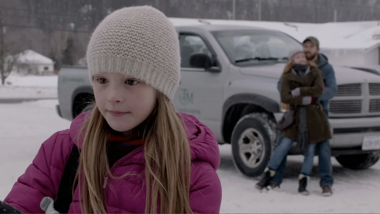 The Captive (2014) movie still: medium — A snow-covered parking lot with a pickup truck parked in the background. A young girl is framed in the…