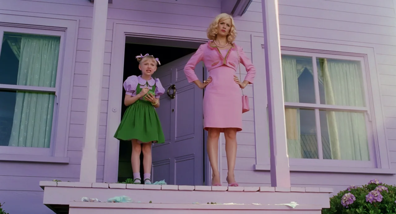 The Cat In The Hat (2003) movie still: fullbody — A pastel-colored house with lavender siding features a wooden front porch and steps. A woman in a…