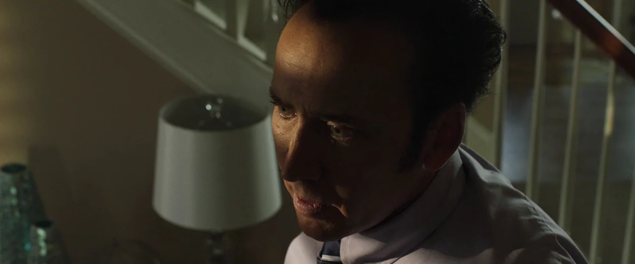 Mom and Dad (2017) movie still: closeup — An interior staircase area with a white banister and a nearby lamp. A man in a dress shirt stands by the…