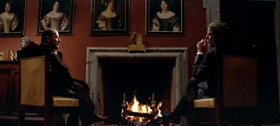 The Leopard (1963) movie still: wide — A dark, wood-paneled room features four framed portraits hanging on a deep red wall. Two men sit in…