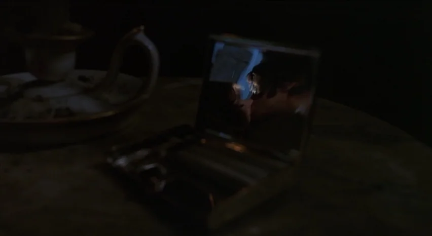 Lisa and The Devil (1973) movie still: closeup — A dimly lit vanity table holds a small open mirror with a reflective surface. The reflection…