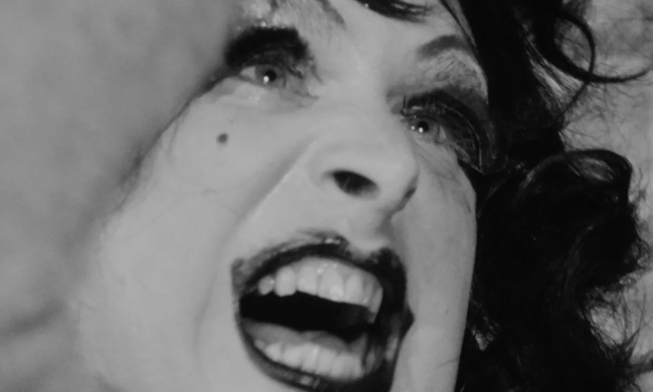 Multiple Maniacs (1970) movie still: closeup — A dark, high-contrast environment frames the tight shot of a person. The individual yells with their…