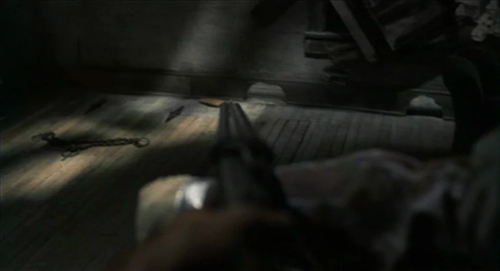 Evil Dead II (1987) movie still: closeup — A rustic interior with wooden floorboards and a piece of metal chain on the ground. A shotgun barrel…