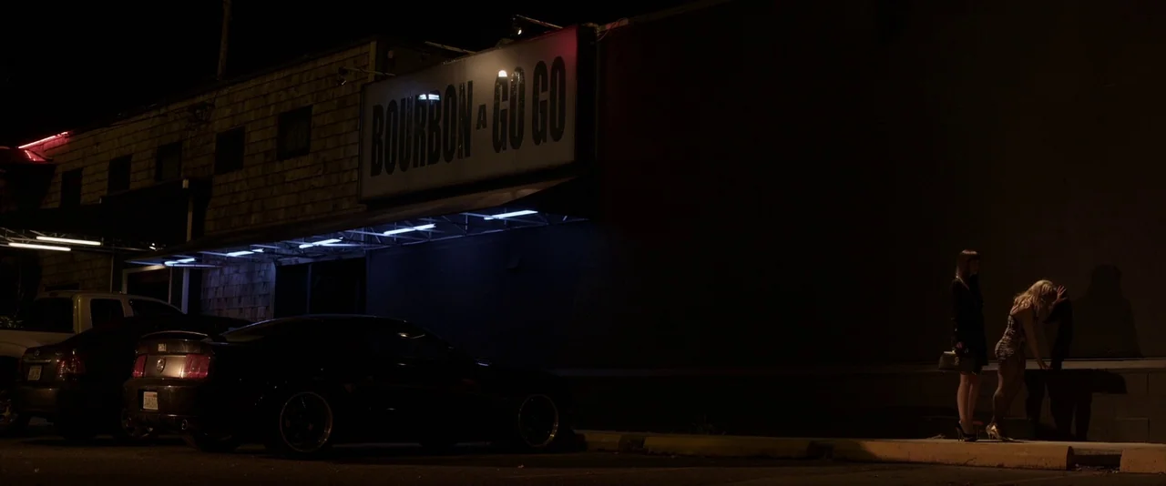 American Mary (2012) movie still: wide — The exterior of a nightclub at night with a large, lit sign overhead. Two women stand near the building…