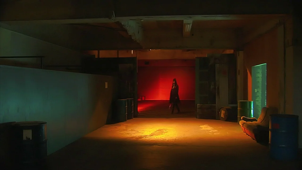 Tokyo Gore Police (2008) movie still: wide — An industrial basement features exposed concrete beams and scattered metal drums in the darkness. A…