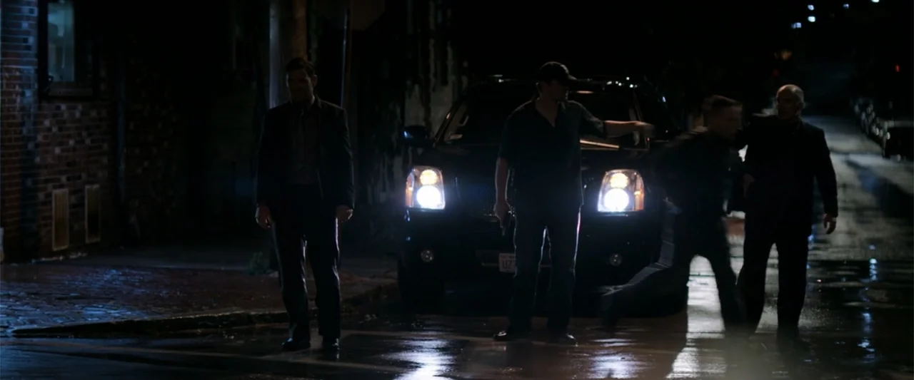 The Equalizer (2014) movie still: wide — A dark urban street at night with a black SUV parked under streetlights. Four men stand in front of the…