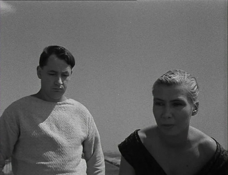 La Pointe Courte (1955) movie still: medium — An outdoor coastal location with a vast, empty sky filling the background. A young man and woman stand…
