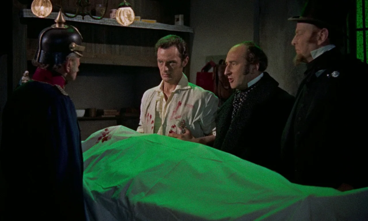 The Revenge of Frankenstein movie still: medium — A dimly lit stone chamber contains a central table covered by a white sheet. Four men in period…