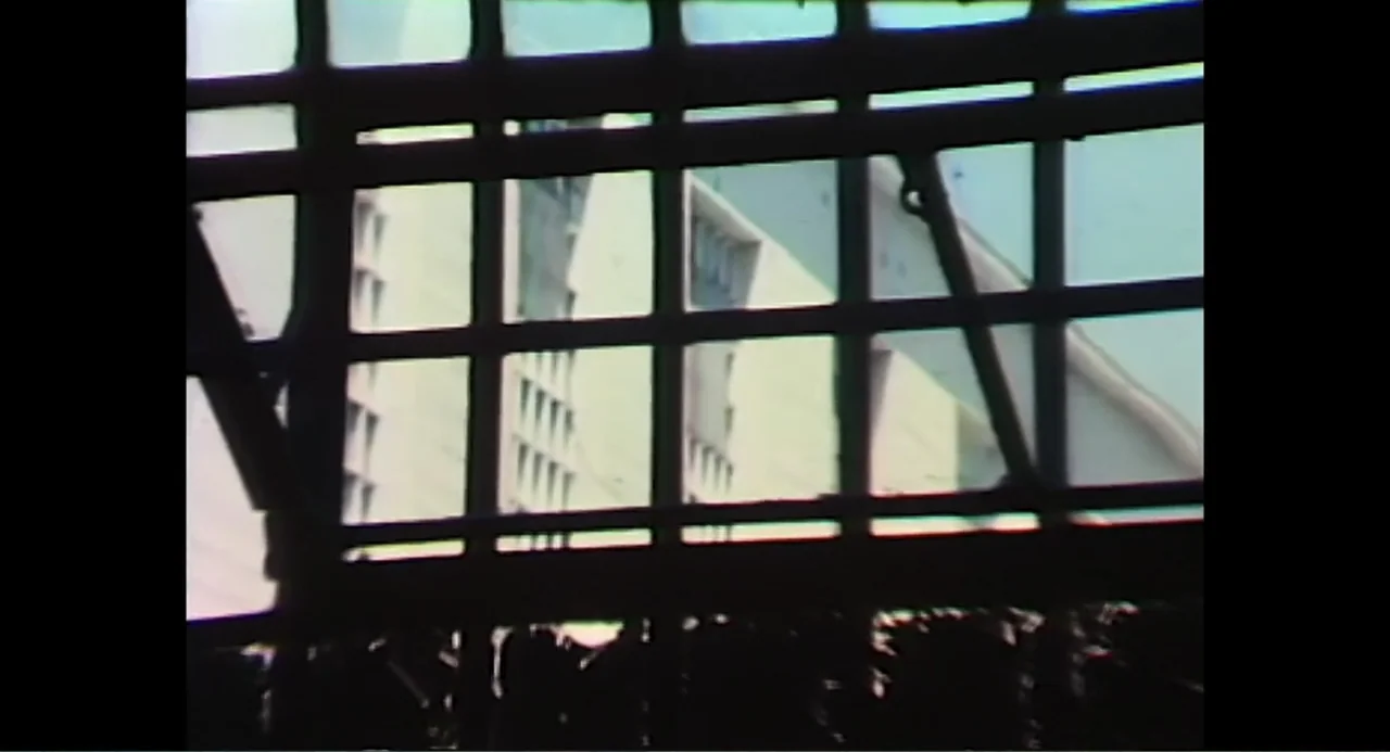 Free Chol Soo Lee (2022) movie still: establishing — A view of a large concrete building seen through a metal barred window. The geometric patterns…