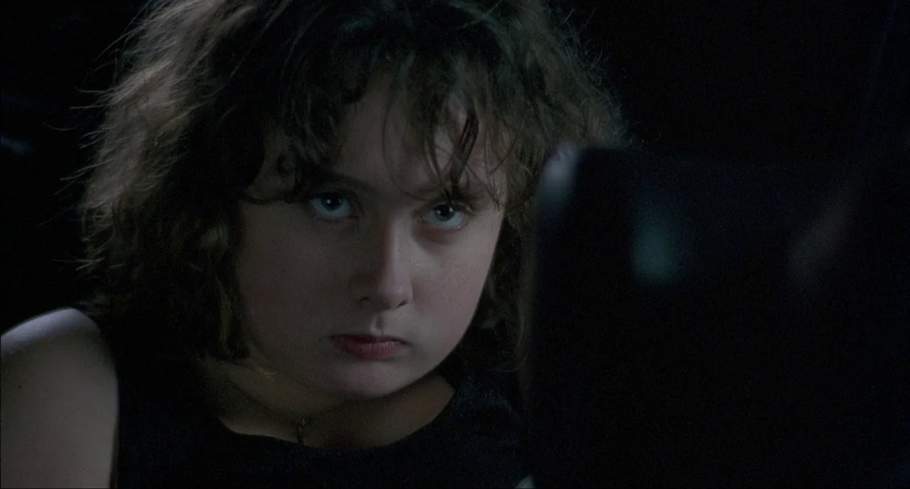 Fat Girl (2001) movie still: closeup — A dark vehicle interior with black surfaces surrounding the subject in low light. A young girl sits in the…