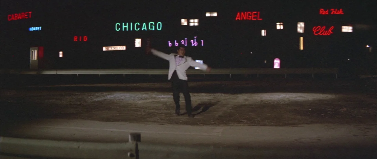 Black Tight Killers (1966) movie still: wide — A dark, sparse asphalt space is illuminated by various multicolored neon signs against a backdrop. A…