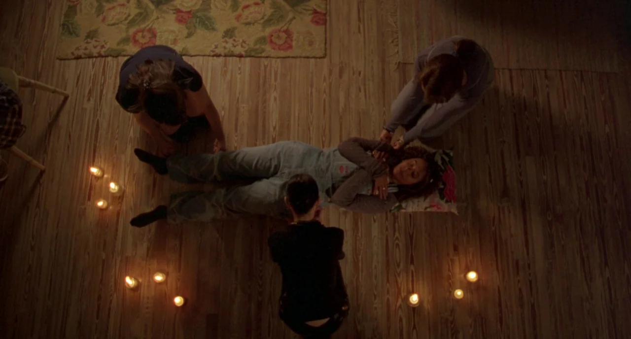 The Craft (1996) movie still: wide — A group of teenagers gather on a wooden floor illuminated by numerous small candles. They encircle a central…