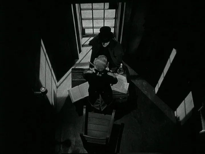 The Black Book (Reign of Terror) (1949) movie still: wide — A dark, sparsely furnished room is illuminated by shafts of light from a window. Two men…