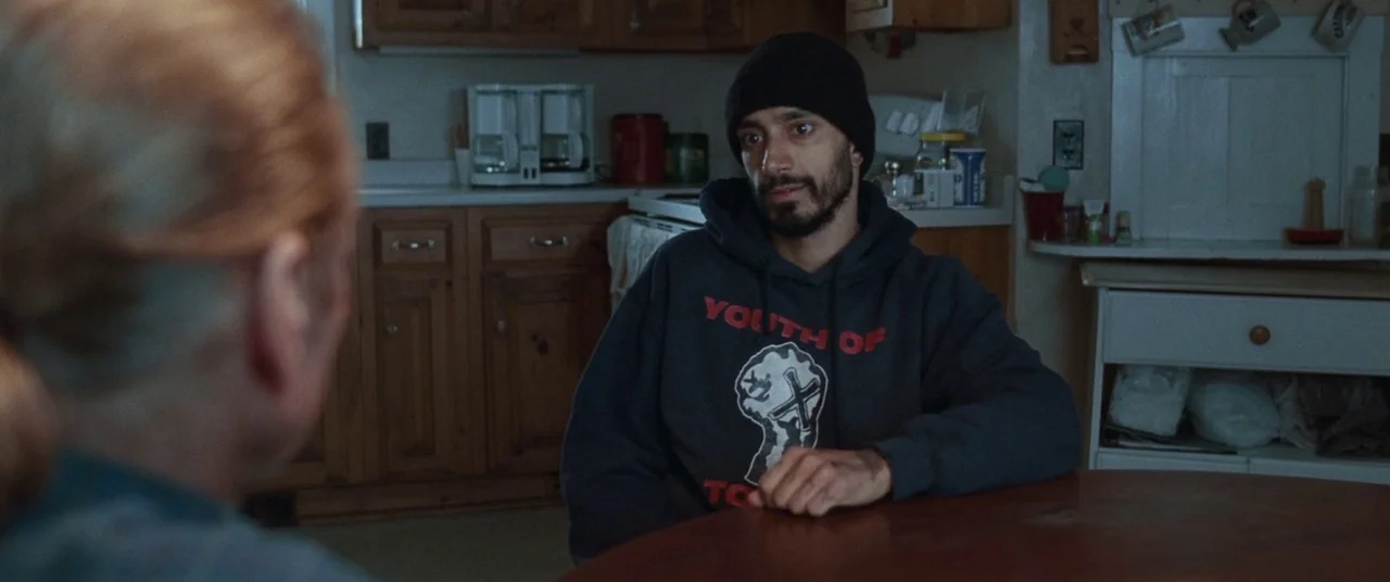Sound of Metal (2019) movie still: medium — A residential kitchen features wooden cabinets and a table where two people sit. A man with a beard…