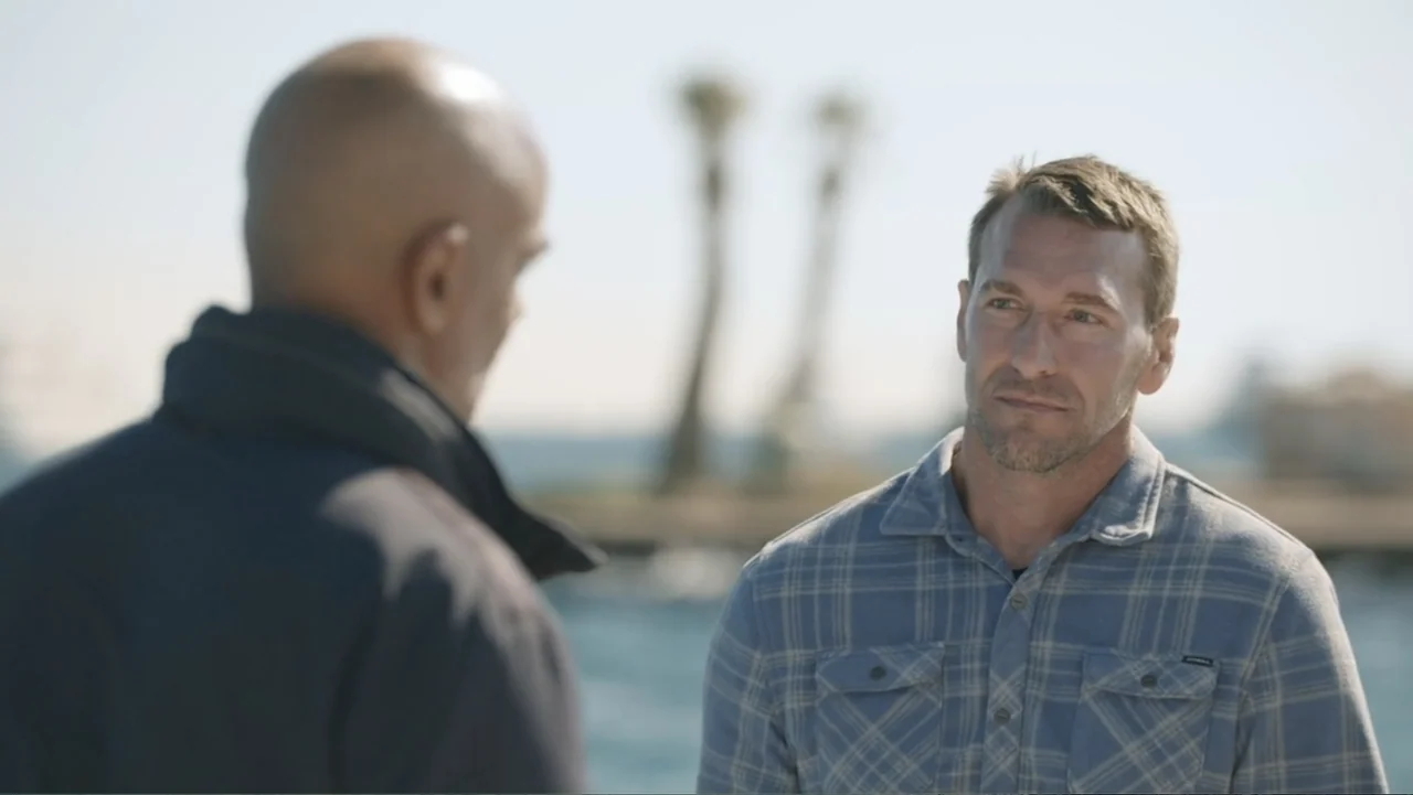 Serial Killer: Red Sea Attacks (2023) movie still: medium — Two men stand near a harbor with palm trees visible in the soft-focus background. The…