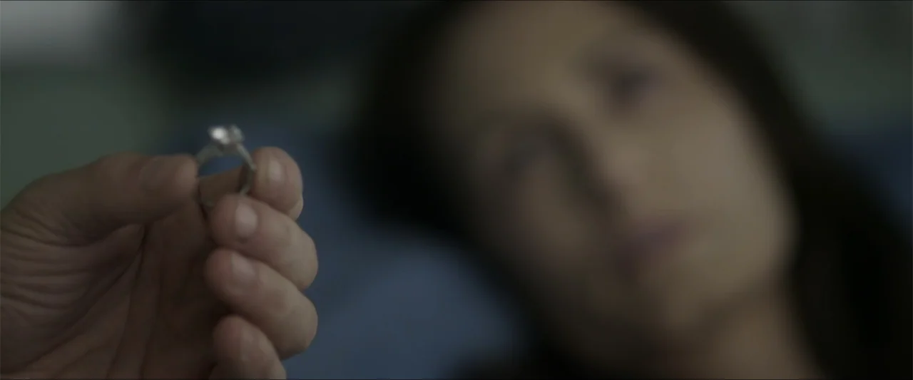 Heavenly Deposit (2019) movie still: closeup — A dark, blurred indoor setting serves as the backdrop. A hand holds a small engagement ring in the…