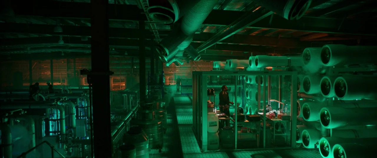 Godzilla Vs. Kong (2021) movie still: wide — An industrial facility features large filtration tanks and exposed ceiling ductwork in darkness. A lone…