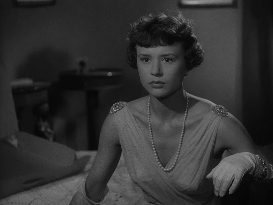 Dreams (1955) movie still: medium — A dimly lit room features a woman sitting at a vanity table. She sits composedly while wearing elegant evening…