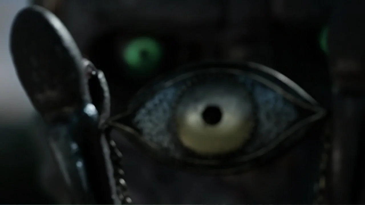 Mortal Engines (2018) movie still: closeup — A detailed eye-shaped pendant with an intricate metal frame rests in the foreground. A dark,…