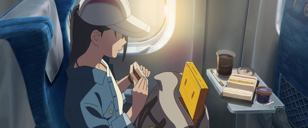 Suzume (2022) movie still: medium — The interior of a train carriage with blue upholstered seats and a tray table. A girl sits by the window holding…