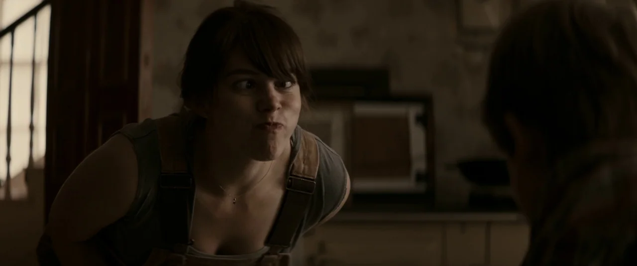 The Hole in the Ground (2019) movie still: medium — A dimly lit room with walls featuring subtle floral patterned wallpaper. A young woman leans…
