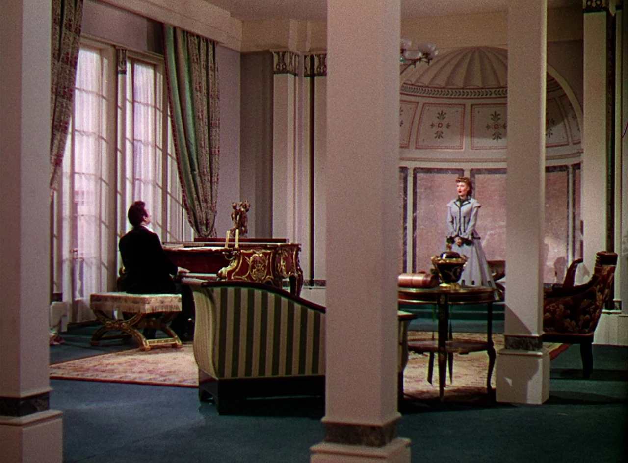 Phantom of the Opera (1943) movie still: wide — An opulent, high-ceilinged room features classical columns and decorative wall panels behind a grand…