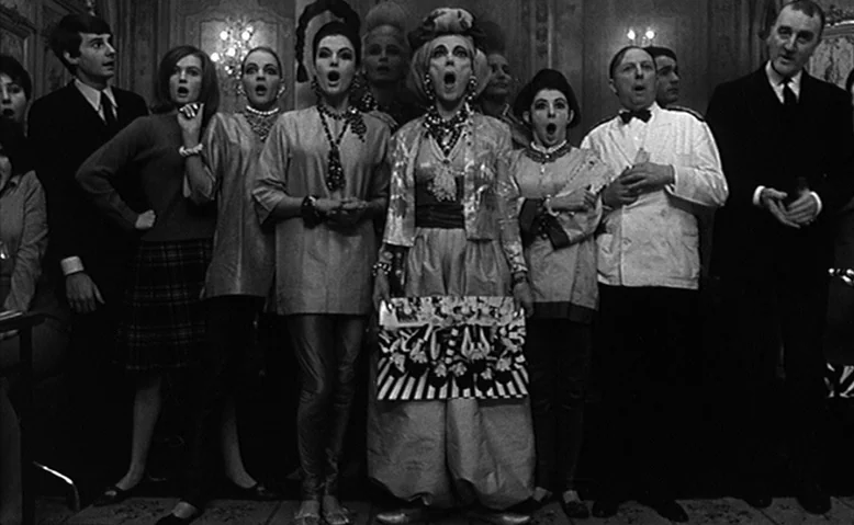 Who Are You, Polly Maggoo? (1966) movie still: medium — A formal interior space features ornate walls and crystal chandeliers in the background. A…