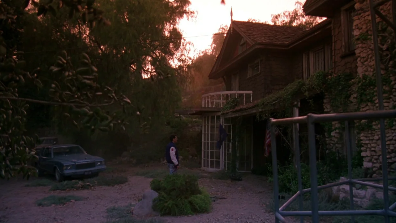 Jason Goes To Hell (1993) movie still: wide — A vintage two-story suburban house sits in a dusty lot during golden hour. A man stands in the…