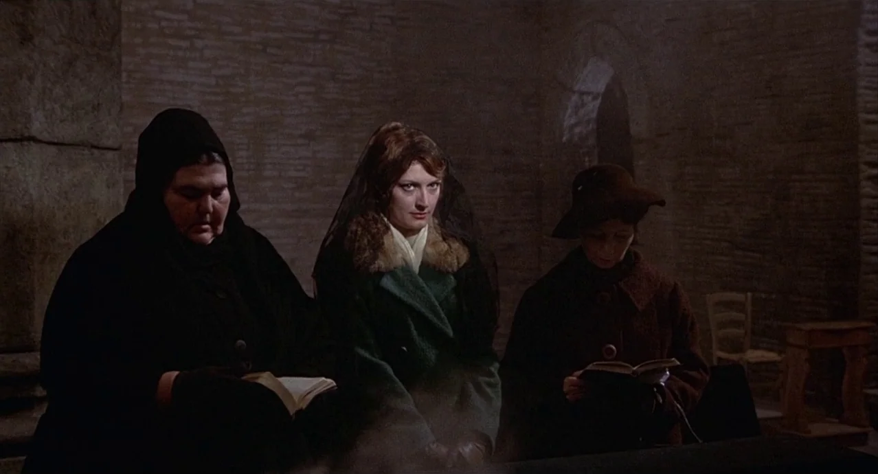 Amarcord (1973) movie still: medium — Three women sit together in a dim stone building with textured brick walls. Each woman holds a prayer book…