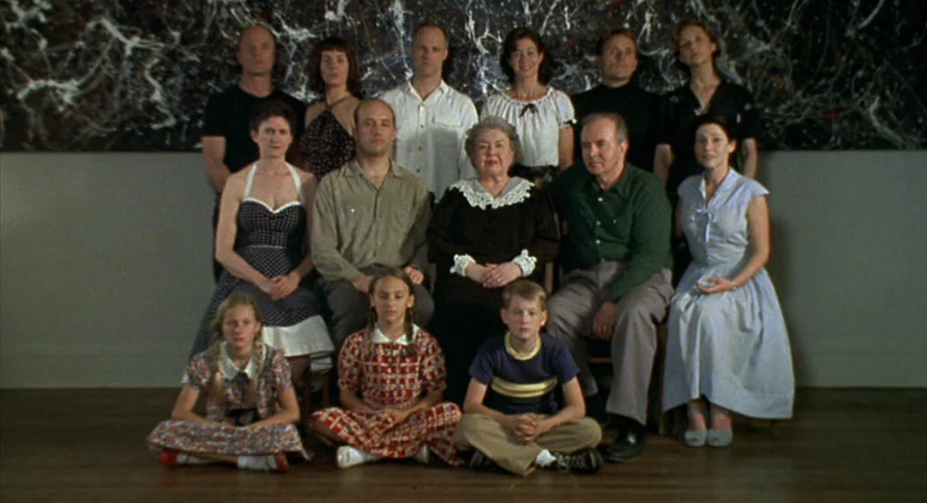Pollock (2000) movie still: wide — A multi-generational family poses for a portrait inside a gallery room. A large abstract drip painting hangs on…