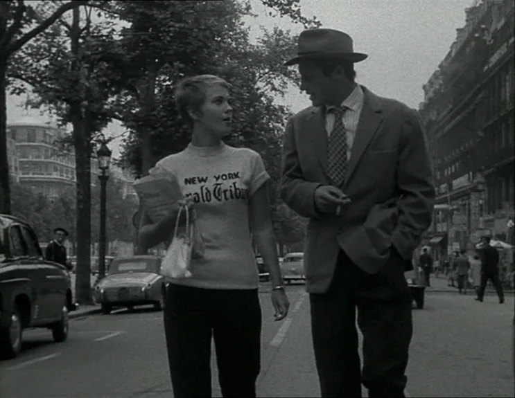 À Bout De Souffle (Breathless) (1960) movie still: medium — A bustling urban boulevard features parked cars and mature trees along the sidewalk. A…