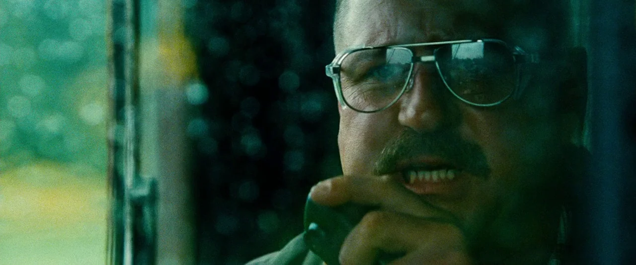 Unstoppable (2010) movie still: closeup — A dark vehicle cab with out-of-focus exterior greenery visible through the window. A man with a thick…